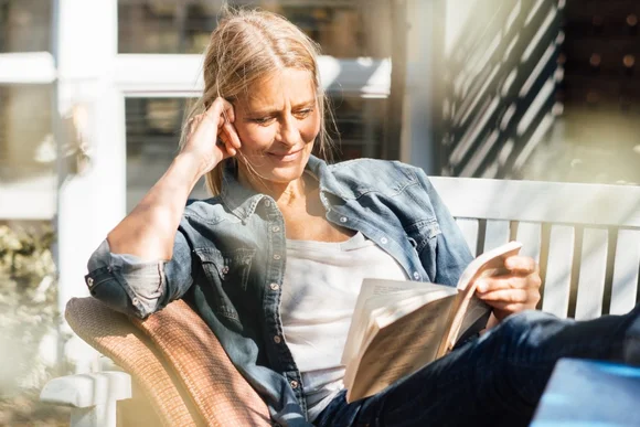 Eine Person sitzt mit einem Buch auf einer Gartenbank